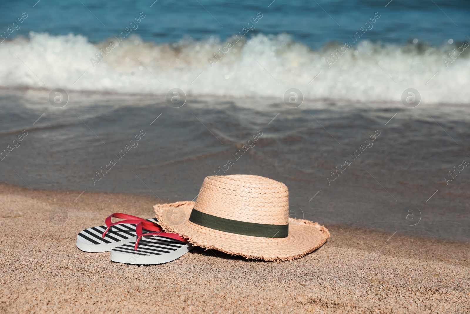 Photo of Striped flip flops and straw hat on sandy beach near sea