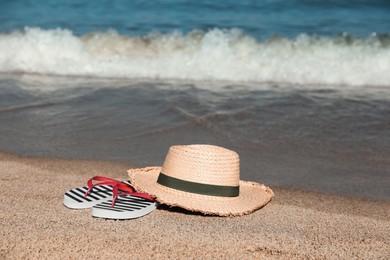 Striped flip flops and straw hat on sandy beach near sea