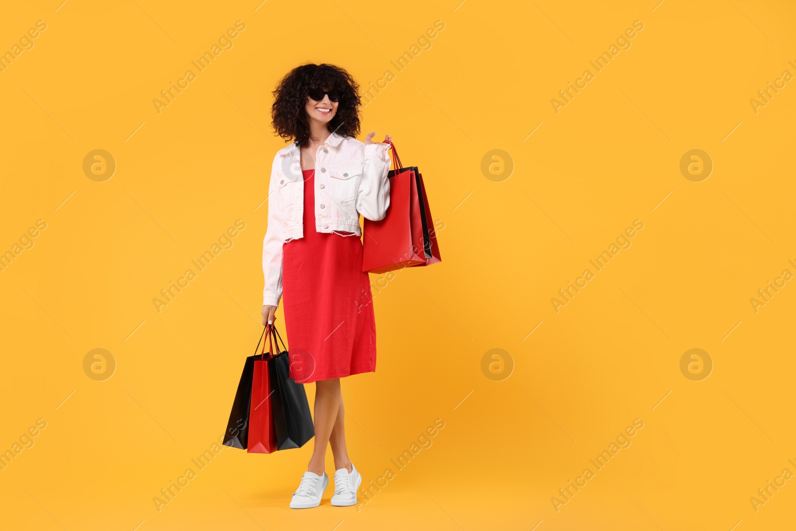 Photo of Happy young woman with shopping bags and stylish sunglasses on yellow background. Space for text