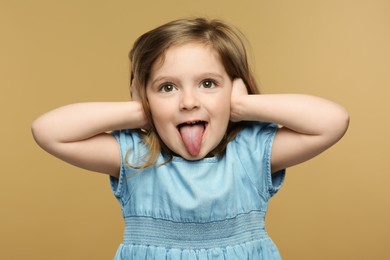 Photo of Emotional little girl showing her tongue on beige background