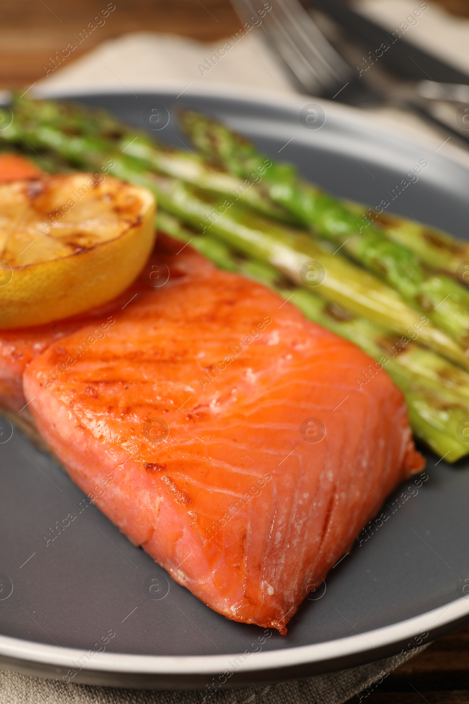 Photo of Tasty grilled salmon with asparagus and lemon on plate, closeup