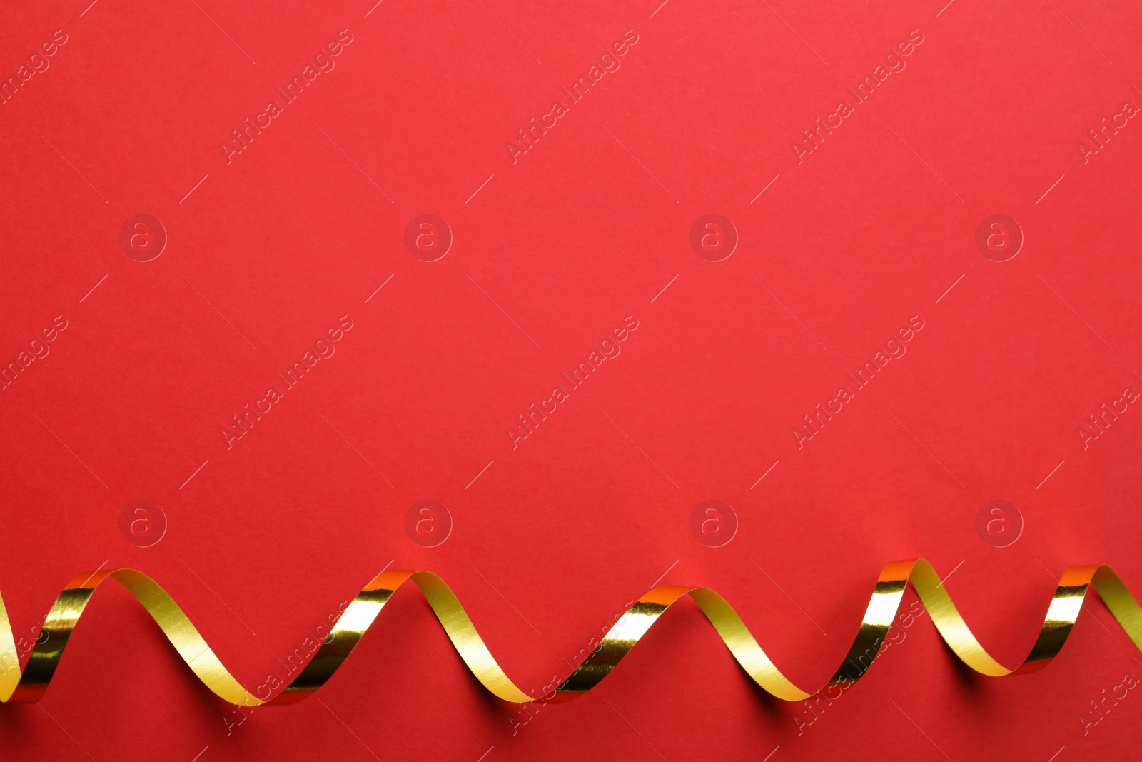Photo of Shiny golden serpentine streamer on red background, top view. Space for text