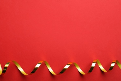 Shiny golden serpentine streamer on red background, top view. Space for text