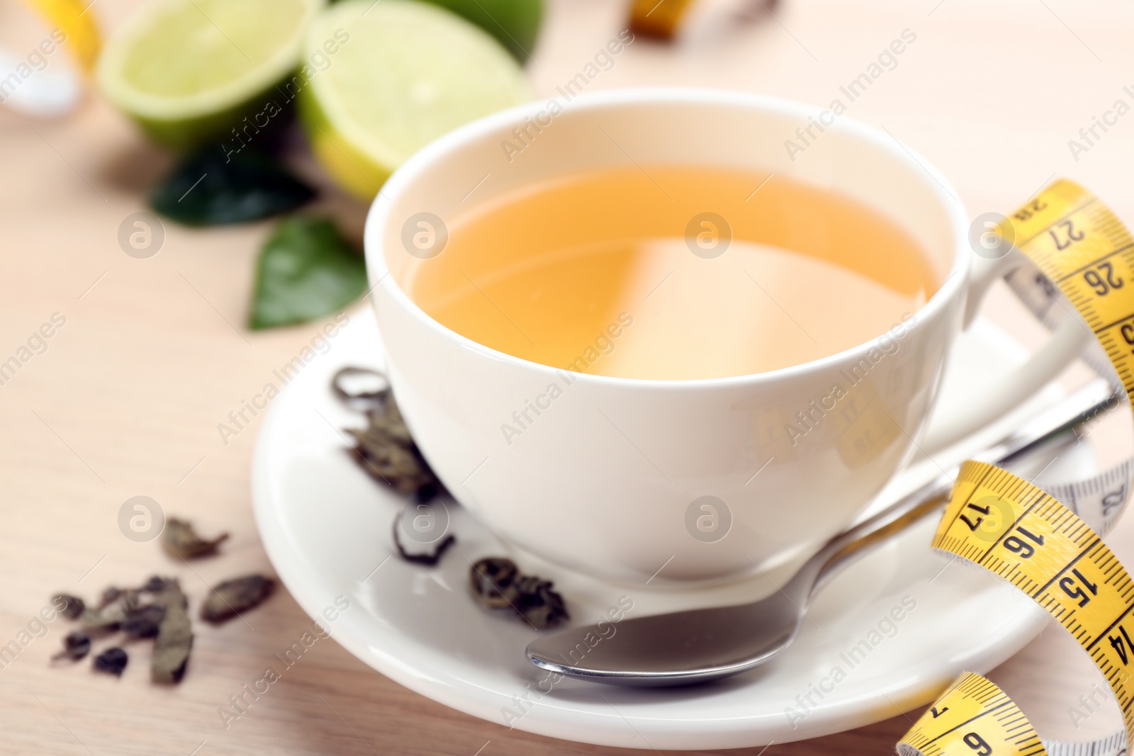 Photo of Cup of diet herbal tea, measuring tape and dried leaves on table, closeup