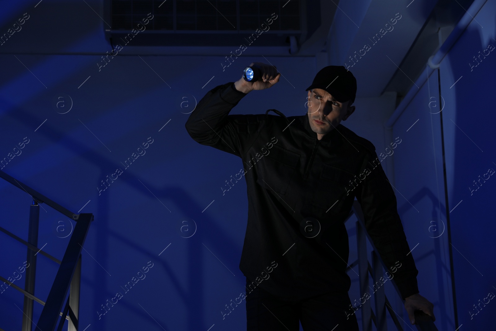 Photo of Male security guard with flashlight on stairs in darkness