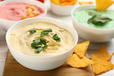 Photo of Different kinds of tasty hummus with nachos on white wooden table, closeup