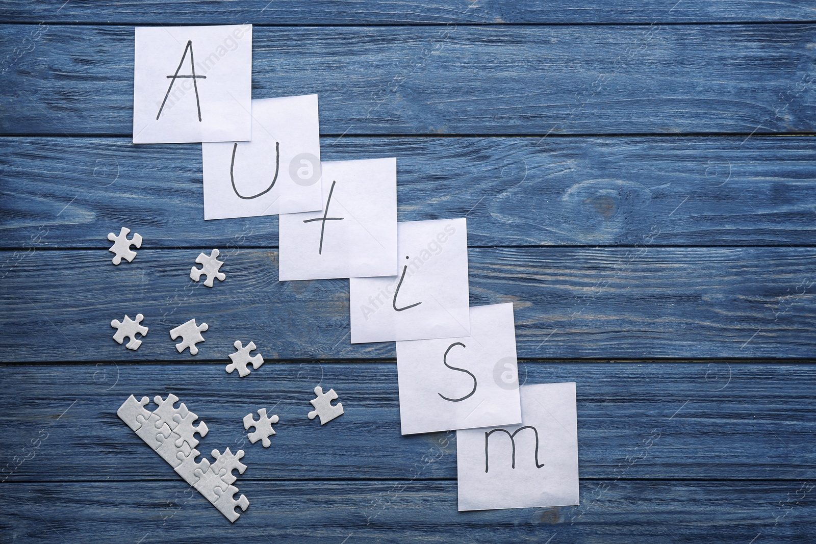 Photo of Notes with word "Autism" and puzzle pieces on wooden background