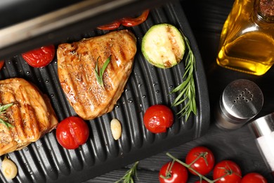 Flat lay composition with electric grill and different products on black wooden table