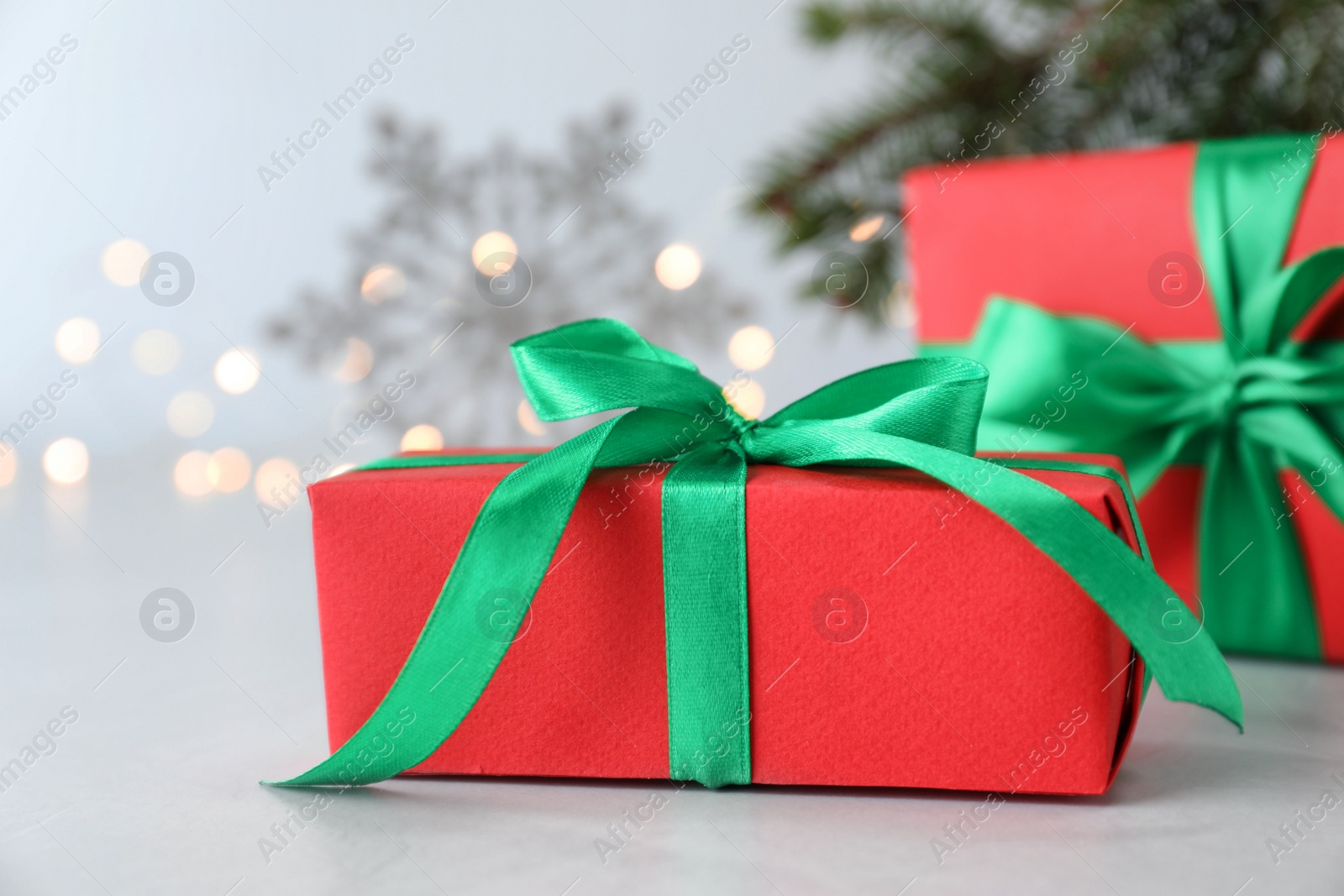 Photo of Christmas gift box with green bow against blurred lights, closeup