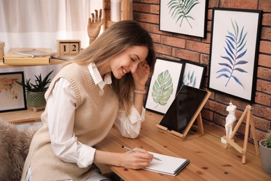 Photo of Young woman drawing in sketchbook with pencil at wooden table indoors