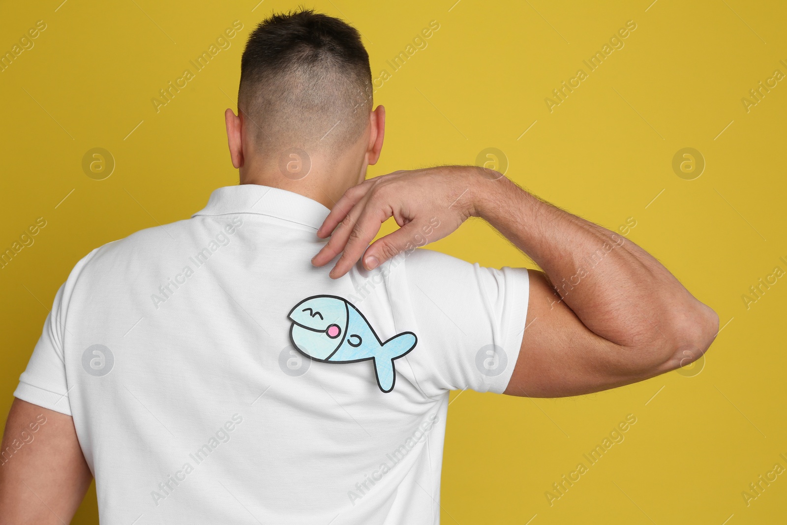 Photo of Man with paper fish on back against yellow background. April fool's day