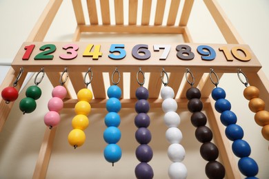 Photo of Montessori toy with color bead lines and numbers on wooden stand near white wall, low angle view