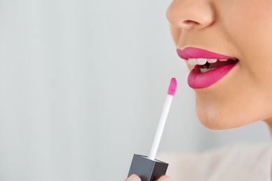 Beautiful woman applying liquid lipstick on light background, closeup. Space for text
