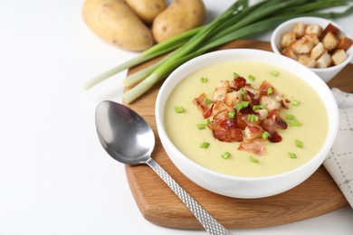 Photo of Tasty potato soup with bacon, green onion and croutons in bowl served on white table, space for text