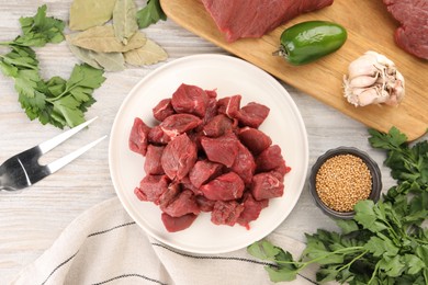 Pieces of raw beef meat, spices and products on light wooden table, flat lay