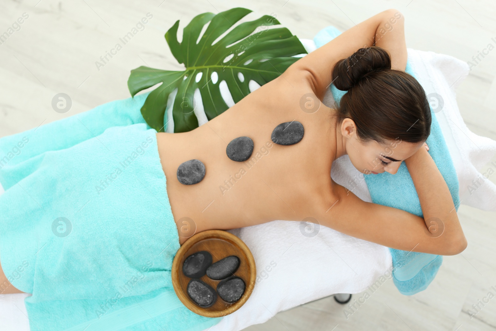 Photo of Beautiful young woman getting hot stone massage in spa salon, top view