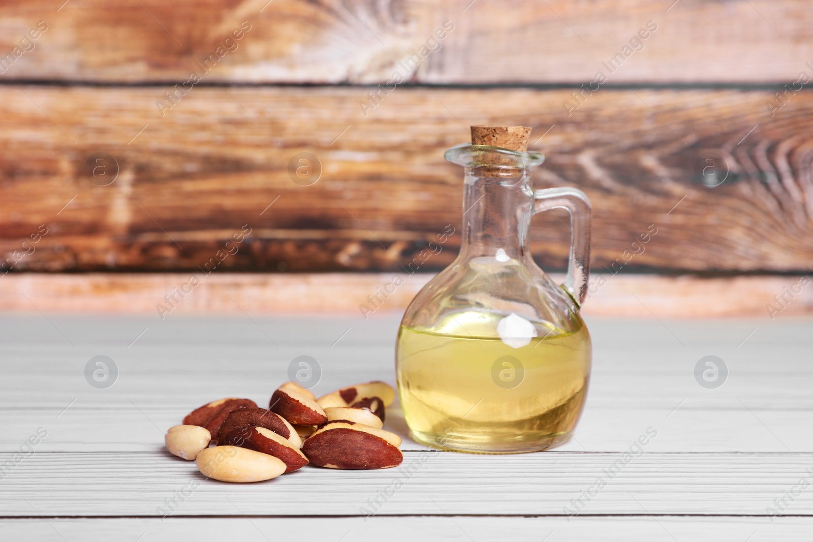 Photo of Tasty Brazil nuts and bottle with oil on white wooden table