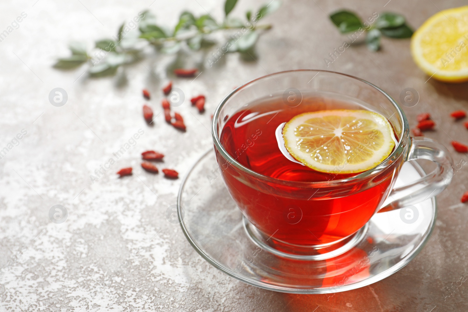 Photo of Glass cup of healthy goji tea with lemon on beige marble table. Space for text