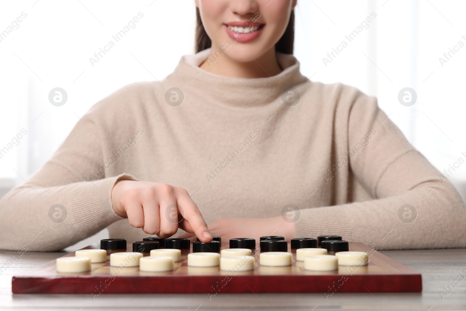 Photo of Playing checkers. Woman thinking about next move at table in room, closeup