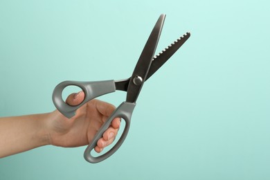 Photo of Woman holding sewing scissors on light blue background, closeup