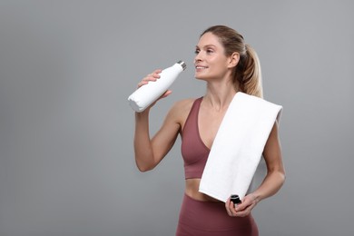 Sportswoman with thermo bottle and white towel on grey background, space for text