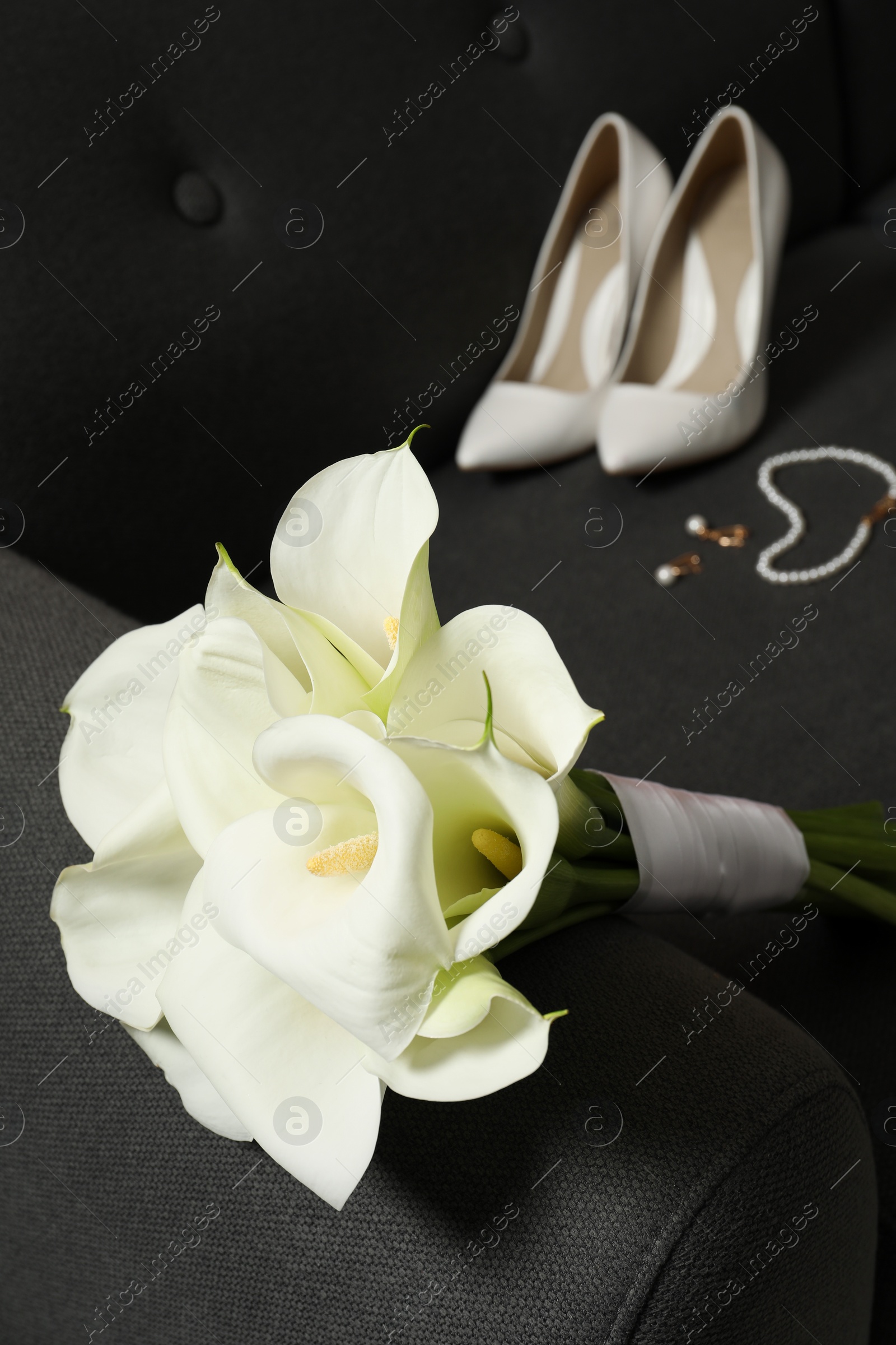 Photo of Beautiful calla lily flowers tied with ribbon, shoes and jewelry on sofa