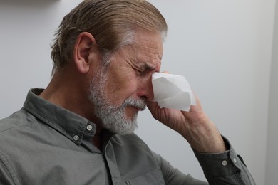 Upset senior man wiping tears with napkin at home, closeup. Loneliness concept