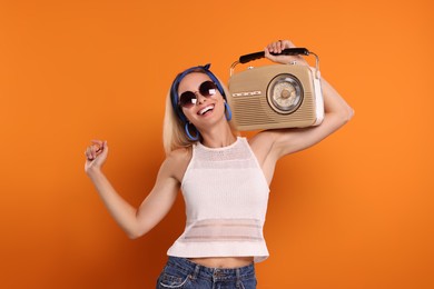 Happy hippie woman with retro radio receiver dancing on orange background
