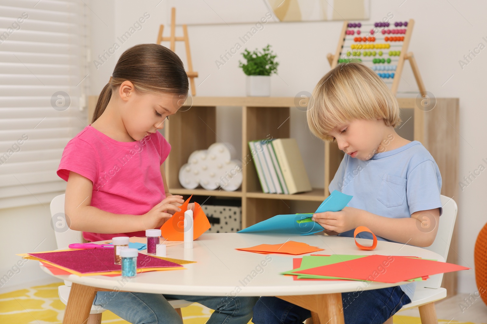 Photo of Cute children making paper toys at desk in room. Home workplace
