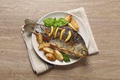 Photo of Tasty homemade roasted crucian carp with garnish on wooden table, top view. River fish