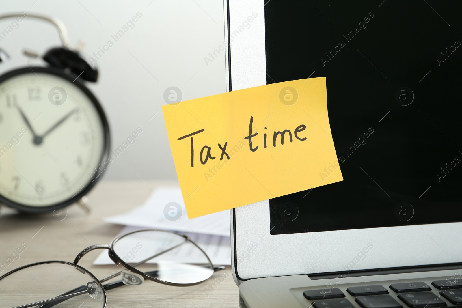 Photo of Reminder note with words Tax Time and laptop on wooden table, closeup