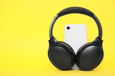Photo of Modern wireless headphones and smartphone on yellow background, space for text