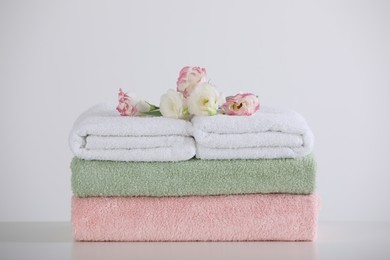 Photo of Soft folded towels with eustoma flowers on white table