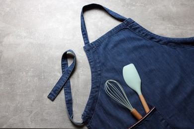 Stylish blue apron, spatula and whisk on grey table, top view. Space for text