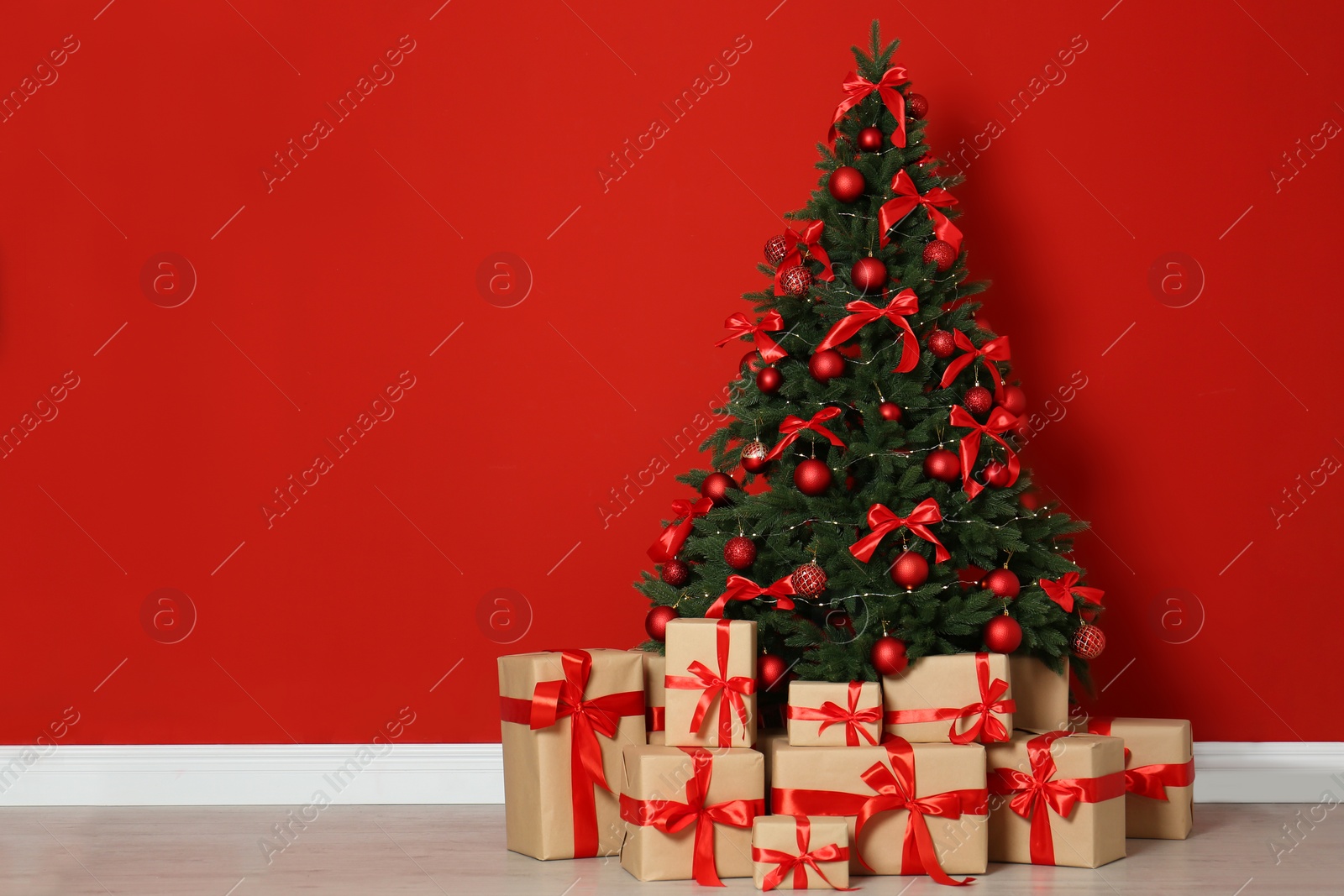 Photo of Decorated Christmas tree and gift boxes near red wall. Space for text