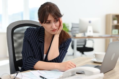 Photo of Overwhelmed office worker sitting at table with laptop and documents indoors