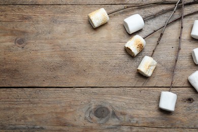 Photo of Sticks with roasted marshmallows on wooden table, flat lay. Space for text