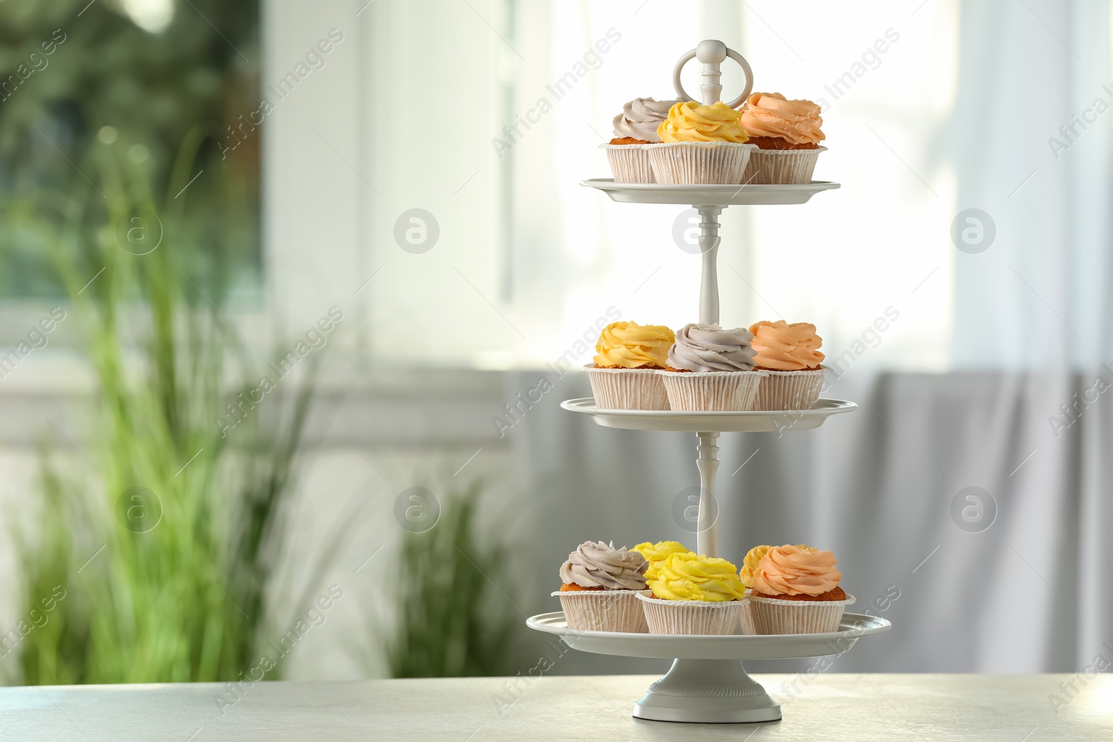 Photo of Dessert stand with tasty cupcakes on white table indoors. Space for text
