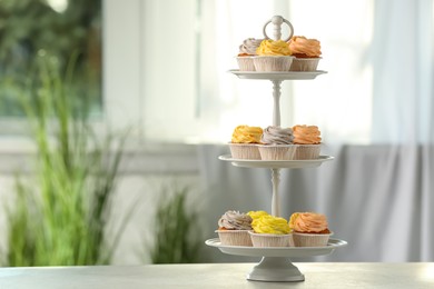 Dessert stand with tasty cupcakes on white table indoors. Space for text