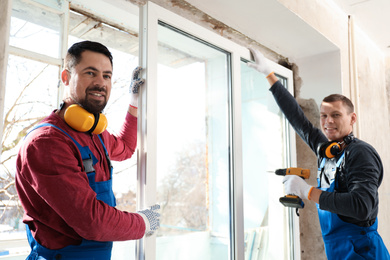 Photo of Workers using electric screwdriver for window installation indoors