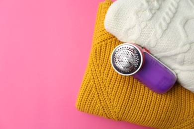 Photo of Modern fabric shaver and woolen sweaters on pink background, flat lay. Space for text