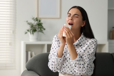 Photo of Suffering from allergy. Young woman with tissue sneezing at home, space for text
