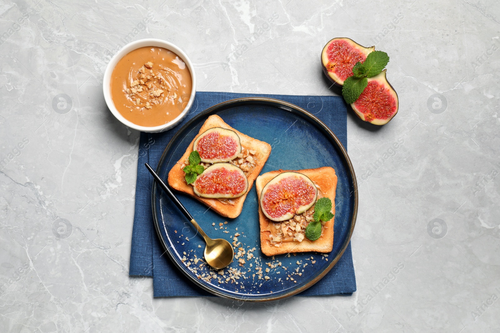 Photo of Tasty toasts served with fig, peanut butter and walnuts on white marble table, top view