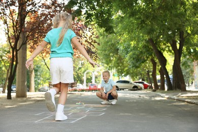 Little children playing hopscotch drawn with chalk on asphalt outdoors