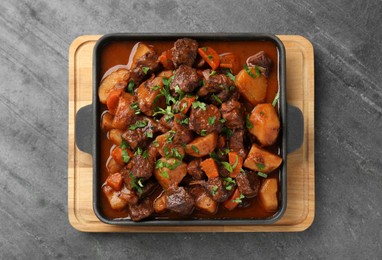 Photo of Delicious beef stew with carrots, parsley and potatoes on grey table, top view