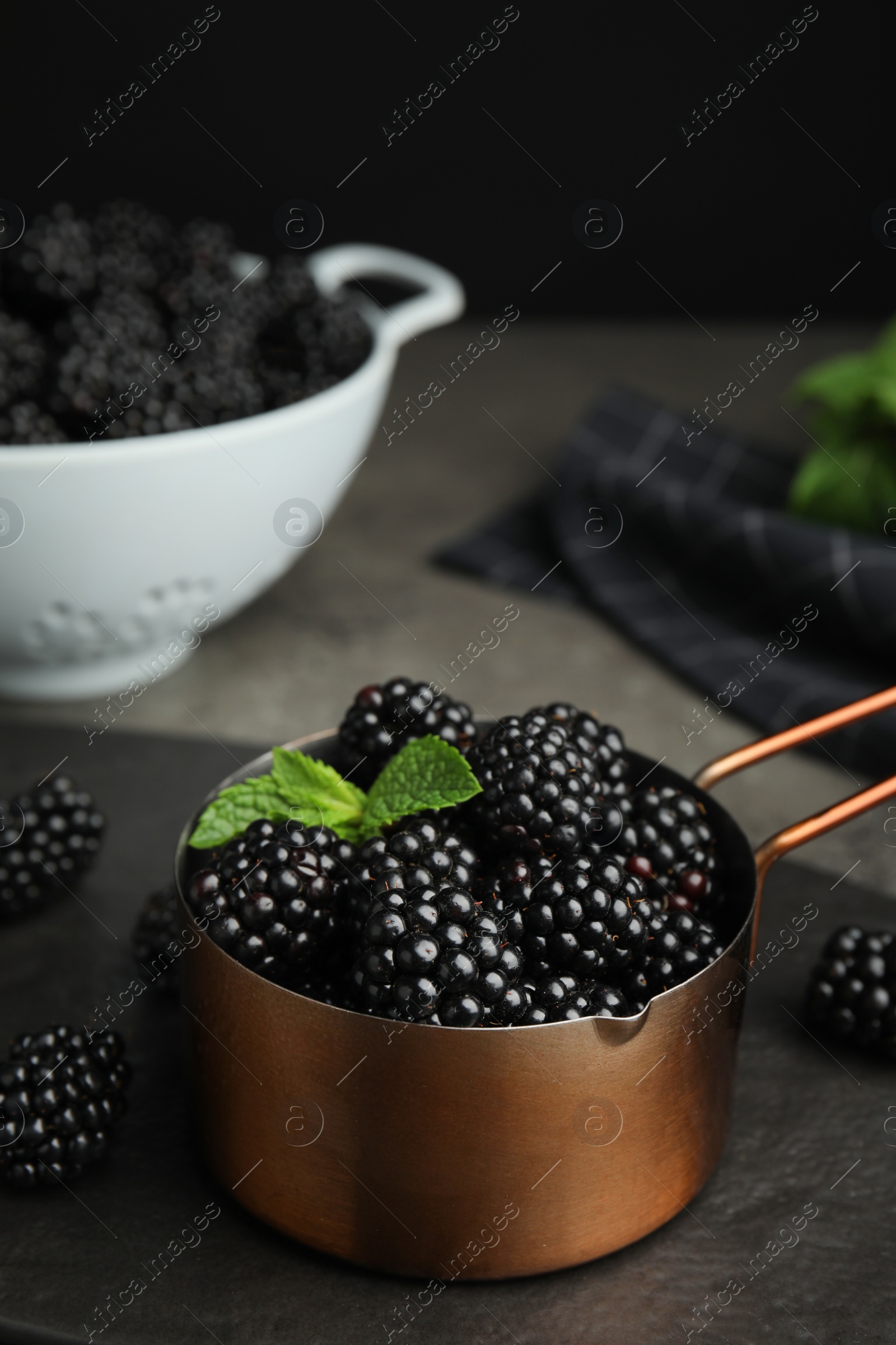 Photo of Metal saucepan with tasty blackberries on grey table