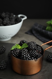 Metal saucepan with tasty blackberries on grey table