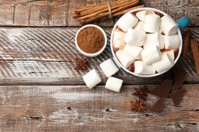 Photo of Tasty hot chocolate with marshmallows and ingredients on wooden table, flat lay. Space for text