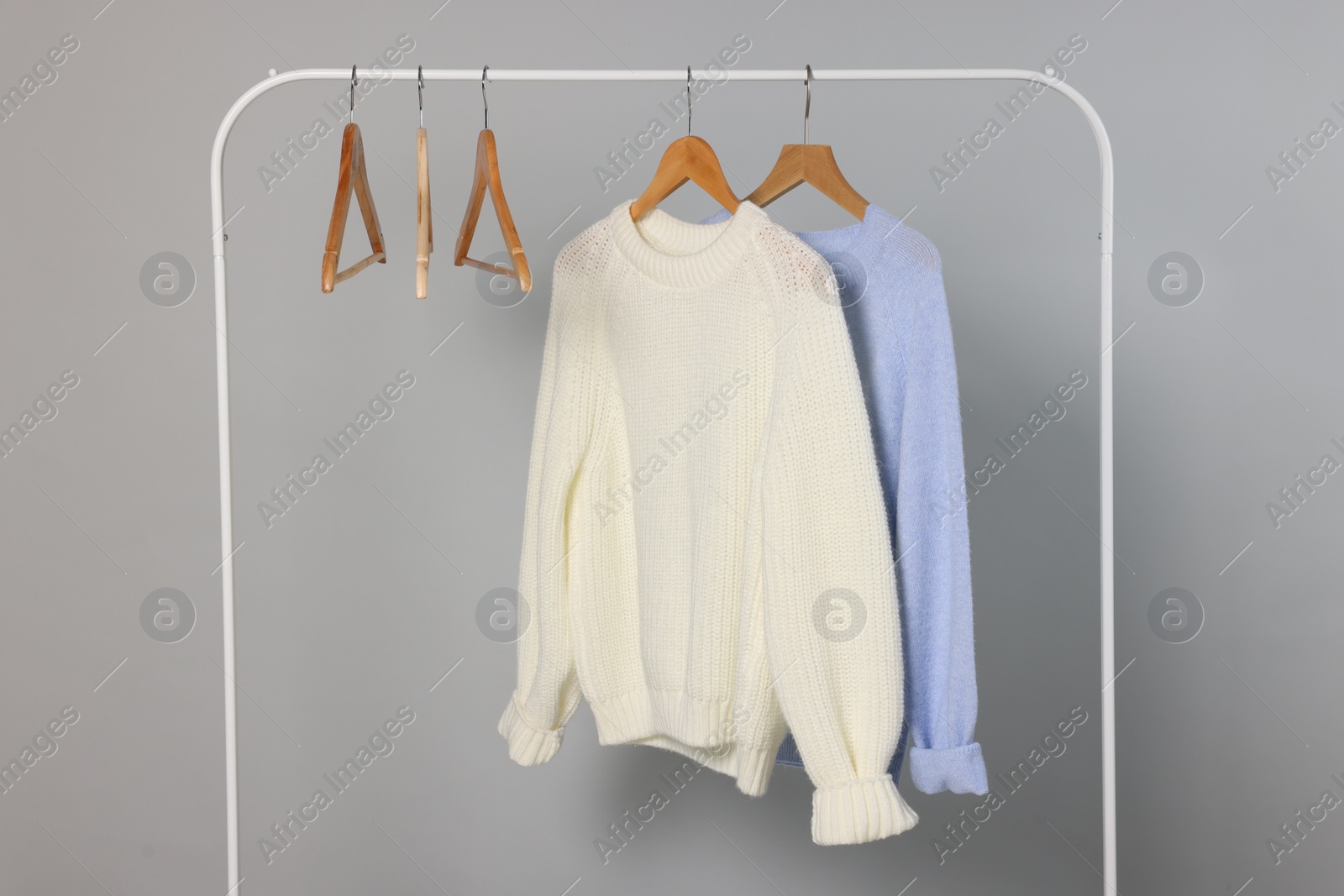 Photo of Rack with warm sweaters and hangers on light grey background