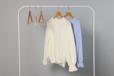 Photo of Rack with warm sweaters and hangers on light grey background